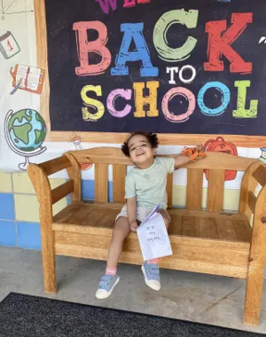 A child sitting on a bench under a Welcome Back to School sign