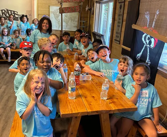 A large group of campers in matching shirts cheering around a long table